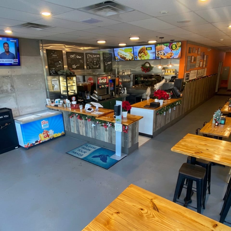 Bright modern restaurant interior with wooden tables, counter service area, menu boards, televisions, and festive holiday decorations.