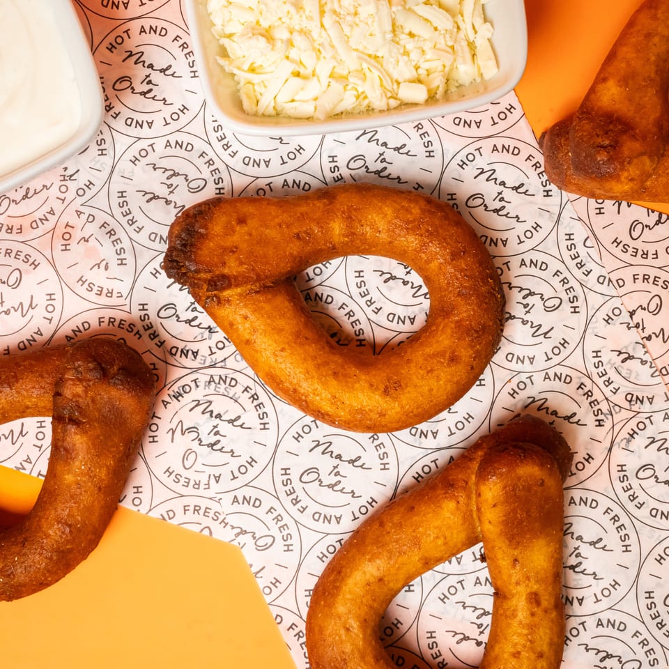 Overhead view of golden fried Venezuelan arepas with orange filling, served with creamy sauce and shredded cheese on branded paper.