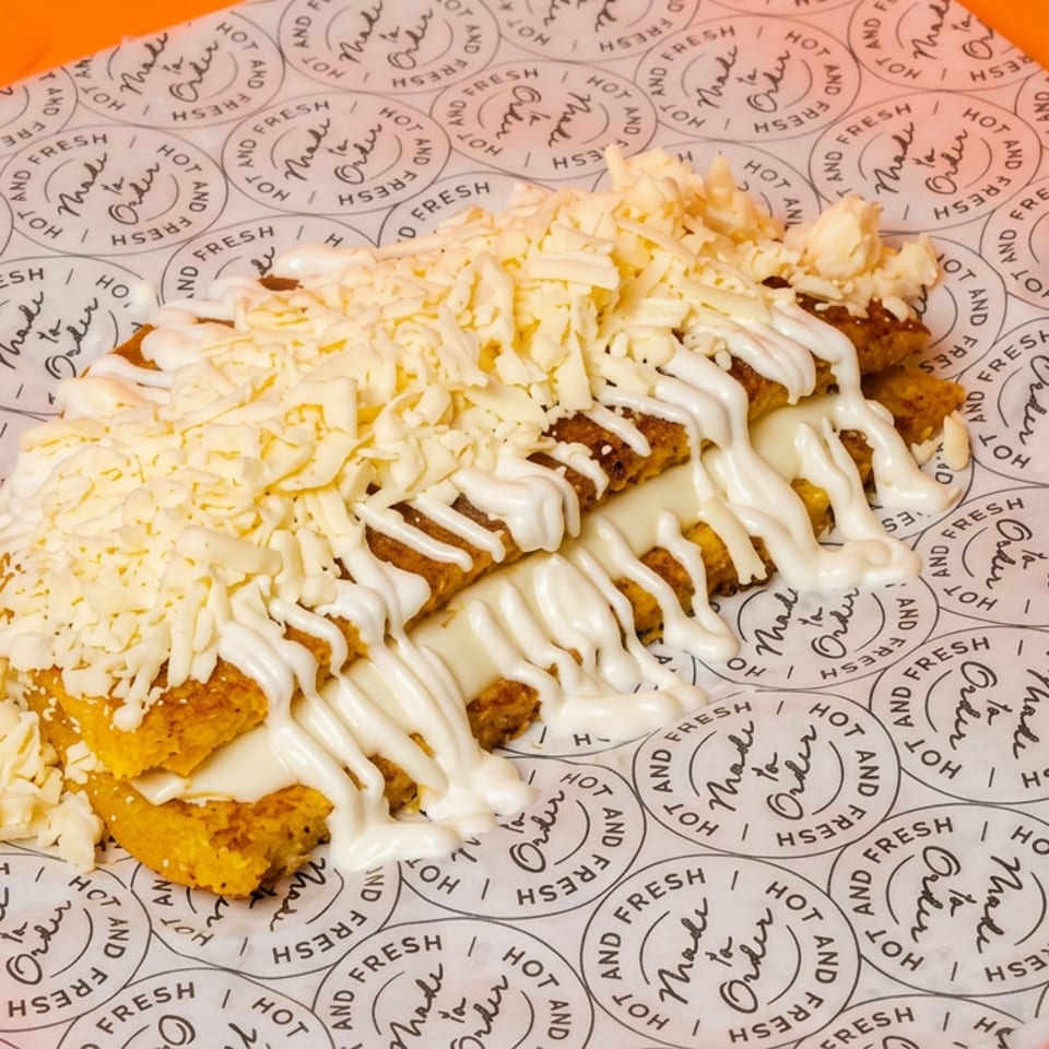 Golden fried rolled pastries topped with shredded cheese and white sauce on branded paper against an orange background.