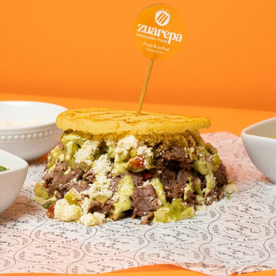 Grilled Venezuelan arepa stuffed with sliced beef, avocado sauce, cheese, and vegetables, served with salsa and creamy dipping sauce.