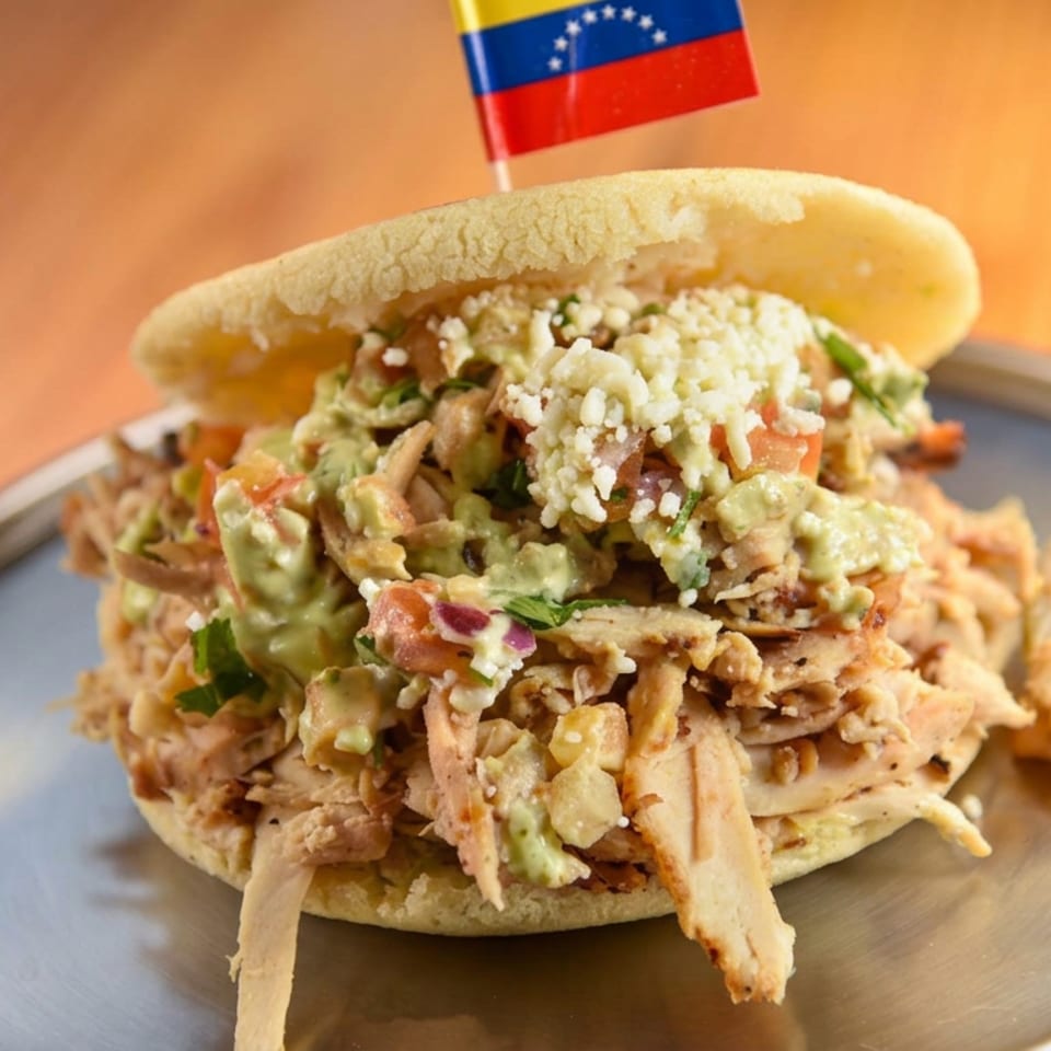 Venezuelan arepa stuffed with shredded chicken, avocado, cheese, and vegetables on a plate.