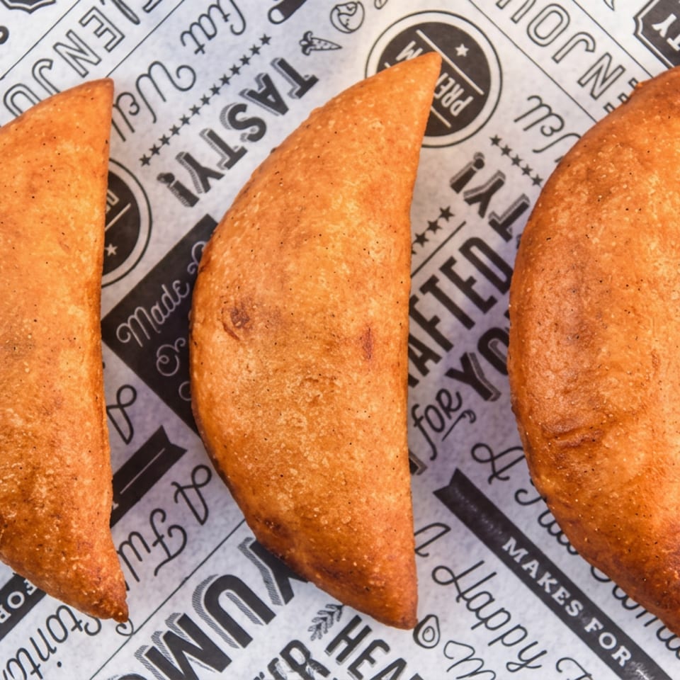 Three golden-brown fried pastries arranged on branded newspaper-style restaurant paper.