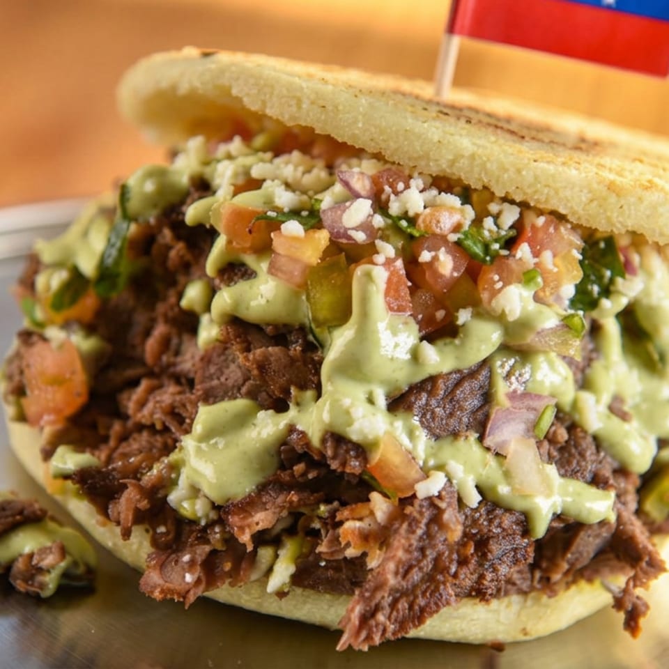Mexican-style sandwich piled with shredded beef, guacamole, pico de gallo, and crumbly cheese on a plate.