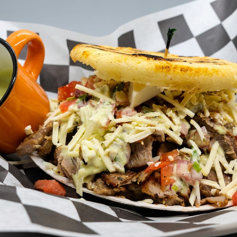 Loaded gyro sandwich with sliced meat, shredded cheese, vegetables, and sauce served with a small cup of creamy dip.